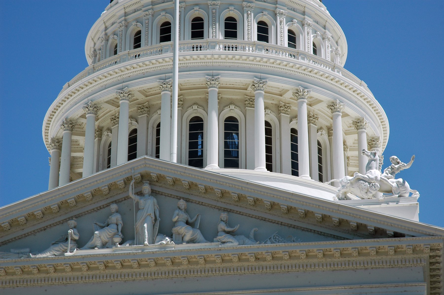 White dome and sculpted pediment of the California State Capitol in Sacramento against a blue sky