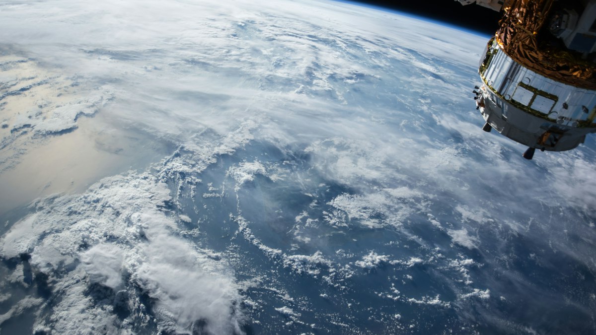 Earth’s cloud-covered surface seen from orbit, with part of a spacecraft at upper right (illustrative; not a Project Suncatcher satellite)