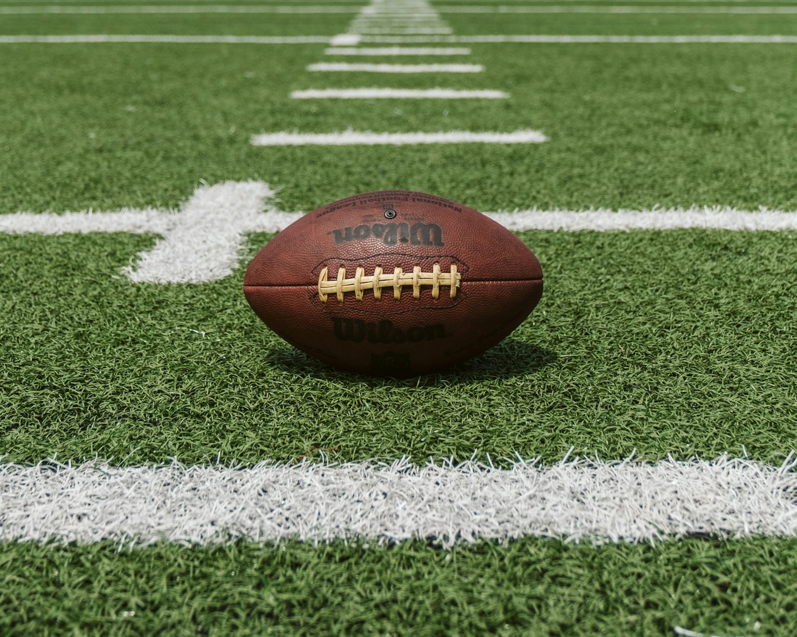 Illustrative image of an American football resting on artificial turf near the yard lines