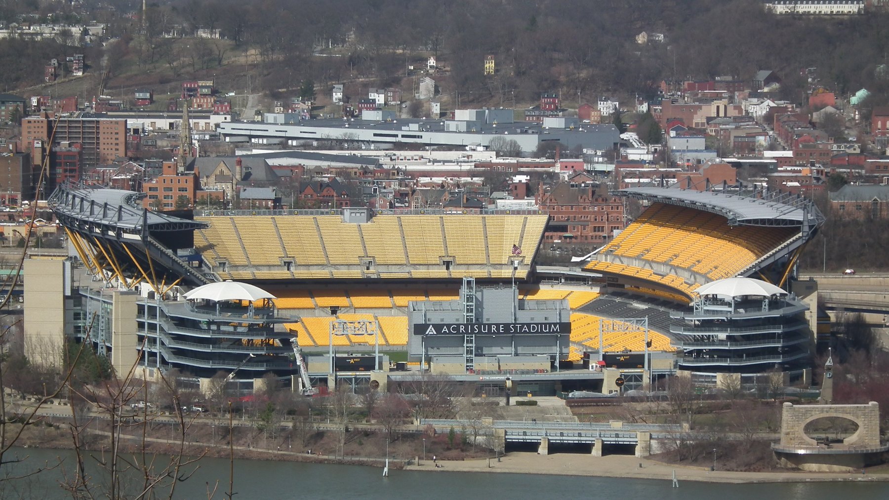 Acrisure Stadium in Pittsburgh, with its yellow seats and “Acrisure Stadium” sign, seen from across the river